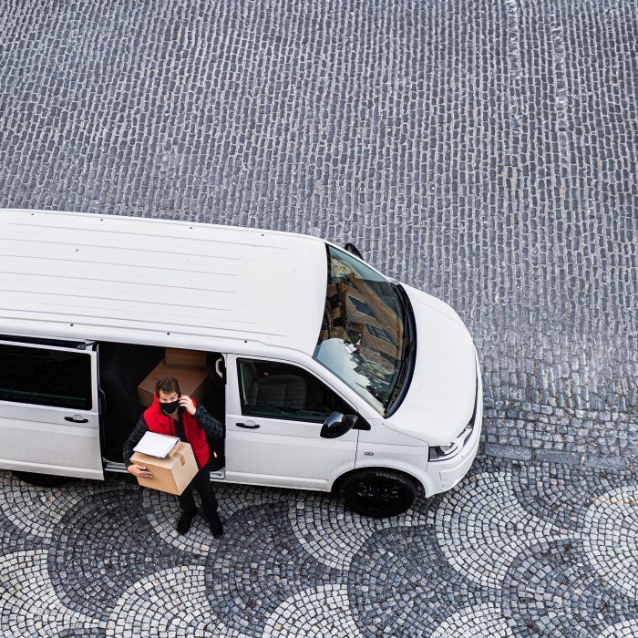 Aerial view of delivery man courier with face mask delivering parcel box in town, using smartphone.