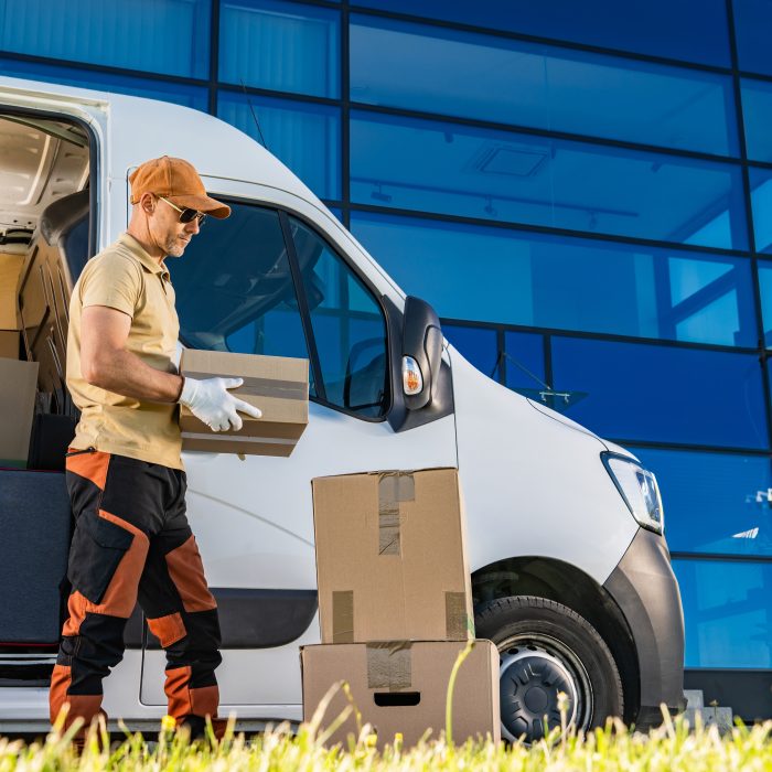 Caucasian courier loading boxes into van in front of building.